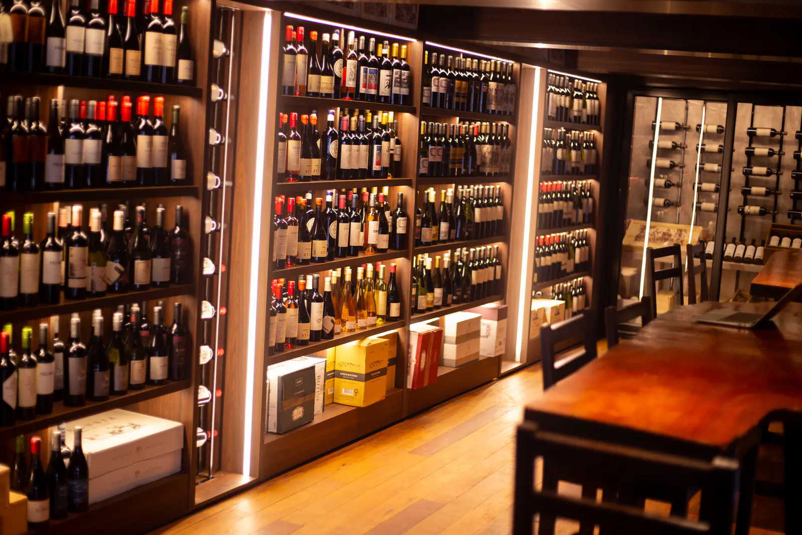 Pared de vinos de la vinoteca con estantes iluminados y mesa de madera