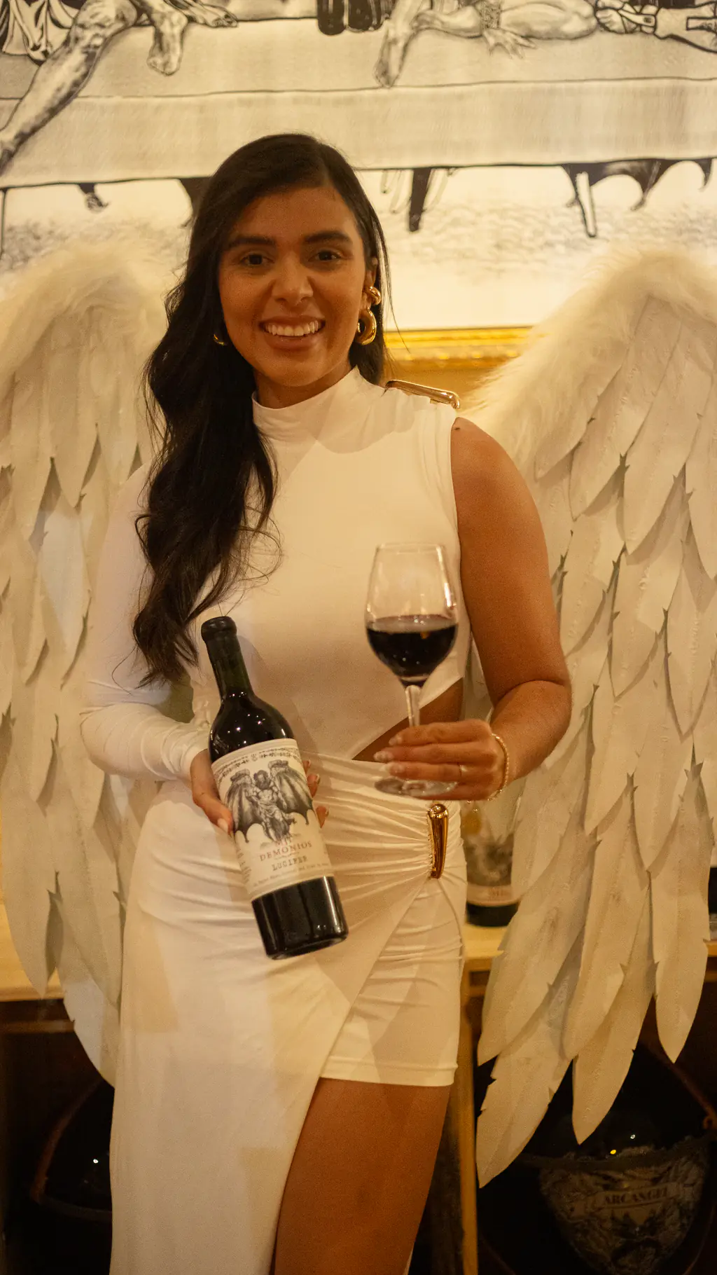 Anfitriona con alas de ángel sosteniendo una copa y un Mil Demonios