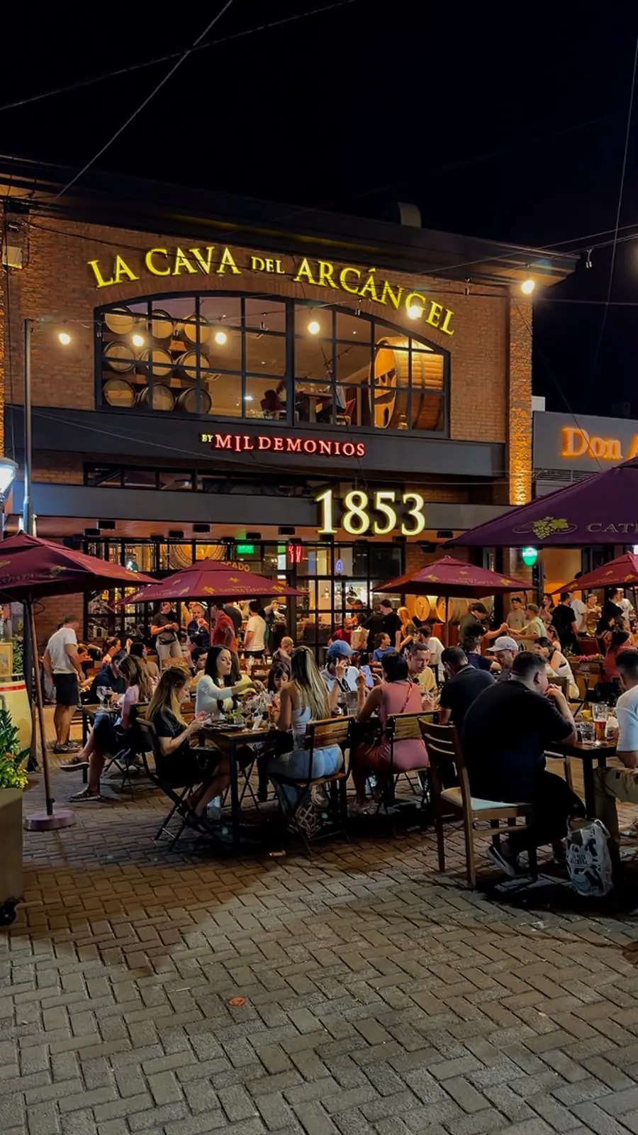 Fachada de La Cava del Arcángel de noche, con la terraza llena